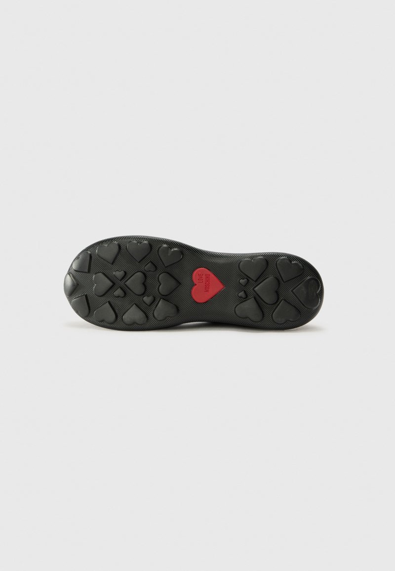 Suola di scarpa in gomma nera con piccoli motivi a forma di cuore e un accento rosso a forma di cuore con il testo "Love Moschino" al centro.