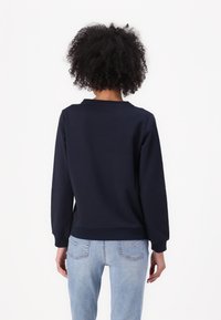 Felpa navy con maniche lunghe e polsini a costine, abbinata a jeans in denim chiaro. Materiale misto cotone. Design semplice, senza pattern visibili.