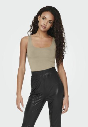 Top de tirantes beige ajustado con escote cuadrado, combinado conleggings brillantes negros de cintura alta. Cabello rizado, accesorios mínimos.