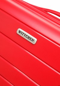 Maleta rígida texturizada de color rojo con ranuras horizontales y una etiqueta de marca plateada "WITTCHEN" en el frente.