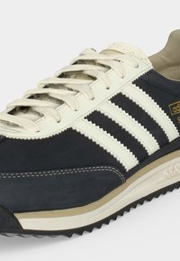 Κοραλλί και λευκό αθλητικό παπούτσι Adidas με τρεις λευκές ρίγες, μπεζ ενδιάμεση σόλα, υφή μαύρης εξωτερικής σόλας και λευκά κορδόνια.