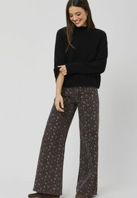 Pull noir en maille associé à un pantalon à jambes larges avec un imprimé animalier foncé. Le tissu semble doux avec une finition texturée et des variations de couleur subtiles.