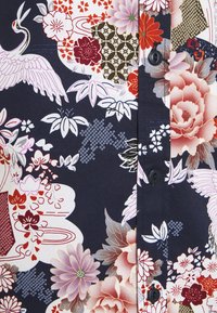 Blauw bloemenoverhemd met een levendige print van rode, roze en witte bloemen, kraanvogels en geometrische patronen; voorzien van zwarte knoopdetails.