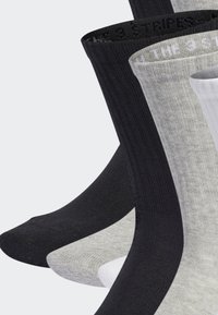 Drei Paar Socken in Crew-Länge in Schwarz, Grau und Weiß. Jeder Socken hat eine gerippte Textur mit kontrastierenden farbigen Sohlen und logoed Bands am oberen Rand.