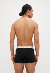 Schwarze Boxer-Shorts mit enganliegendem Design, elastischem weißen Bund mit dem Text "Copenhagen Studios", aus Baumwollmaterial mit glatter Textur.