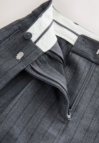 Szürke csíkos nadrág fehér belső derékpánttal. Gombos záródással, cipzáras sliccel és gondosan varrott részletekkel rendelkezik.