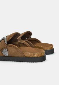 Sandali in suede marrone con una soletta in sughero, dotati di una suola in gomma nera e di accessori metallici decorativi sul cinturino.