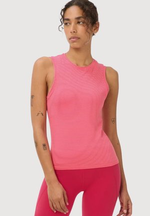Vrouw draagt een mouwloos roze gestreept topje en bijpassende roze legging, staat met zichtbare tatoeages op armen tegen een effen achtergrond.