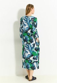Blumenmuster, knöchellanges Kleid in Grün-, Blau- und Schwarz-Tönen. Verfügt über lange Ärmel, Taschen und einen lockeren Schnitt.