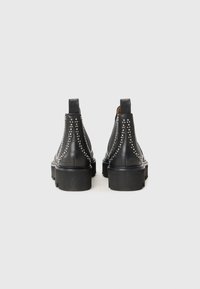 Botas de tobillo de cuero negro con acentos de tachuelas plateadas, punta redonda y suela gruesa de goma. Incluyen bucles de tirón para facilitar su colocación.