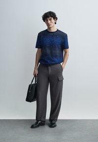 Navy blue short-sleeve shirt with a textured pattern, paired with gray wide-leg cargo pants featuring side pockets and a black bag.