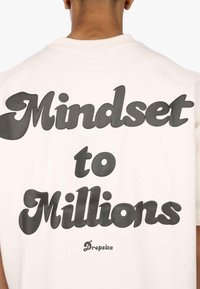 Lyserød t-shirt med fed, sort tekst, der står "Mindset to Millions" og mærket "Dropsize" i mindre skrift. Kortærmet design.