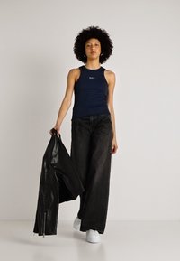 Marine blå tank topp med en tett design, kombinert med svarte vide jeans. Modellen holder en svart skinnjakke og har på seg hvite sneakers.