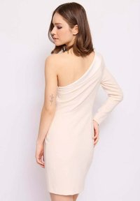 Abito bodycon corto beige con scollatura asimmetrica, manica lunga su un lato, tessuto liscio e design minimalista.