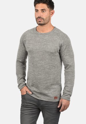 Sweatshirt tricoté gris avec un col rond, des manches longues et une finition texturée. Doté d'un petit patch en cuir avec un logo sur le bas.