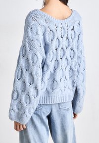 Light blue knitted sweater with a loose fit, featuring large open stitch patterns, wide sleeves, and a ribbed hem.