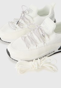 Sneakers bianchi Versace Jeans Couture con lacci a fantasia, suole nere e lacci bianchi extra su uno sfondo bianco.