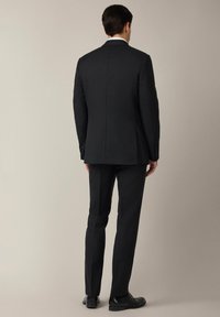 Czarny dopasowany garnitur z jednym rozcięciem, proste spodnie i eleganckie czarne buty. Gładki materiał i czyste linie tworzą formalny wygląd.