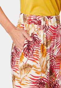 Pantalons légers à motif floral avec une large ceinture élastique, présentant des motifs de feuilles rouges, orange et jaunes sur un fond crème.