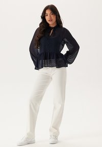Blusa peplum blu navy con tessuto trasparente e strutturato, maniche lunghe a palloncino, bottoni sulla parte frontale e un fiocco al colletto.