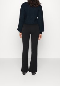 Black flared pants made of stretchy material, paired with a navy blue textured sweater. Both garments have a fitted silhouette and long sleeves.