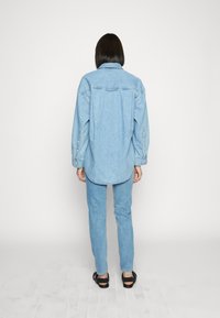 Vaaleansininen farkkupaita rentoa kokoa, pitkät hihat ja napit hihansuissa, yhdistettynä samansävyisiin vaaleansinisiin farkkuihin ja mustiin sandaaleihin.