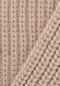 Beżowy, dziany materiał o prążkowanej teksturze i miękkim, puszystym wyglądzie, z wyraźnymi pionowymi i ukośnymi wzorami ściegów.