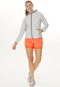 Lys grå hættetrøje med lynlås foran og lommer, parret med klare orange shorts. Begge dele har et sporty design og pasform.