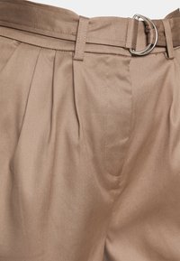 Beige hoge taille broek met riemlussen, plooien aan de voorkant en een stoffen riem die is vastgemaakt met een zilveren dubbele D-ring gesp.