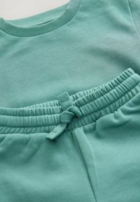 Lys teal sweatshirt og joggers med ribbet rund halsudskæring og en elastisk talje med en bindedetalje. Blødt, tekstureret stof.