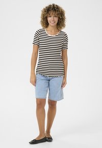 Prúhovaný čierno-biely top s krátkym rukávom a zúbkovaným výstrihom, kombinovaný s svetlomodrými denim bermudami a čiernymi plochými topánkami.