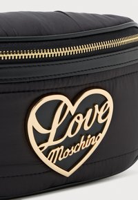 Fekete steppelt táska arany cipzárral és szív alakú arany logóval, amelyen a "Love Moschino" felirat olvasható. Simaságával és fényes részleteivel tűnik ki.