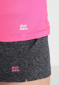 Růžové sportovní tričko s mřížkovou texturou a bílým logem, spárované se šedými šortkami s jemným vzorem a růžovým logem na lemu.