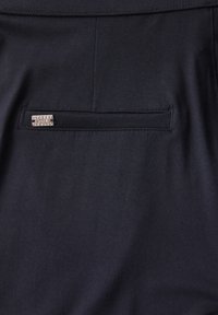 Černá tkanina, hladký povrch, na zadní kapse se nachází malá stříbrná obdélníková visačka s označením „STREET“, doplněná o výrazné švy.