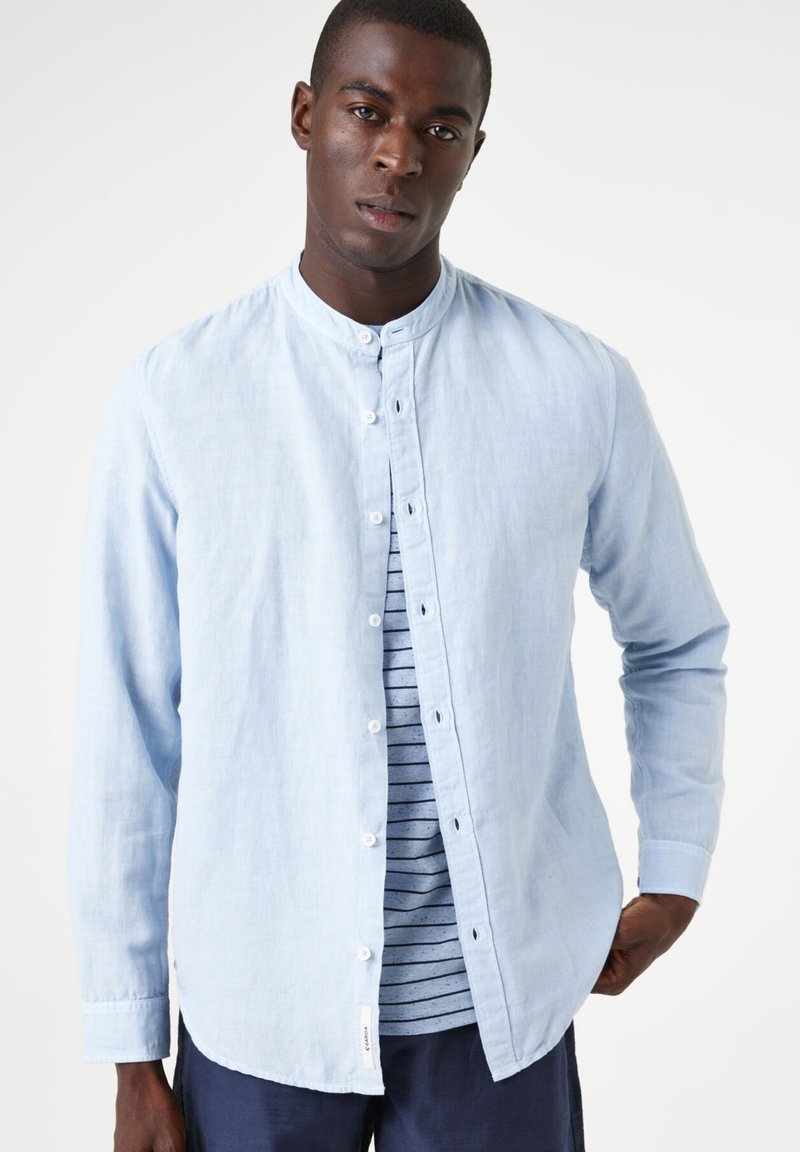 Lichtblauw overhemd met lange mouwen, knoopsluiting en een bandkraag, gemaakt van zachte stof. Gelaagd over een gestreept t-shirt met ronde hals en een subtiel patroon.