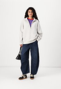 Light gray fleece pullover with a half-zip collar, paired with loose-fitting dark denim pants and black sneakers with light soles.
