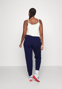 Navy joggers with a tapered fit, elastic waistband, and side pockets, paired with a white camisole and athletic shoes.