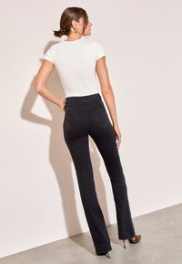 Črne široke kavbojke z visokim pasom, petimi žepi in gladko teksturo, kombinirane z oprijetim belim kratkim rokavom.