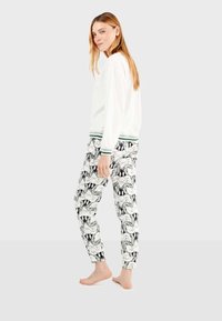 Weißer Sweatshirt mit grünen gestreiften Bündchen und gemusterten Schlafanzughosen mit schwarz-weißen Cartoon-Gesichtern, schlanker Schnitt, entspannter Look.