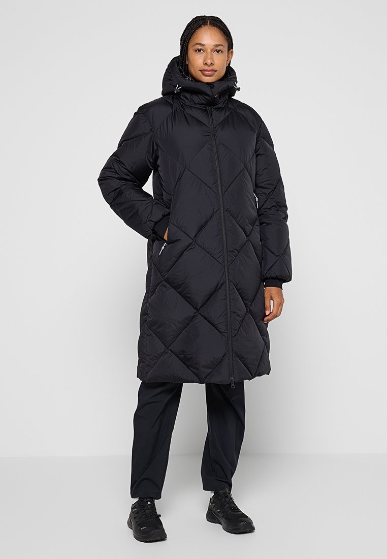 Schwarze Daunenjacke mit einem Rautenmuster, hohem Kragen, Reißverschluss und Taschen. Trägt sie über schwarzen Hosen und Sneakers.