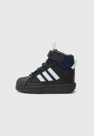 Sort og navy højtop-sneaker med hvide striber, snørelukning foran, velcrolukning og tekstureret sål, vist fra siden på en hvid baggrund.