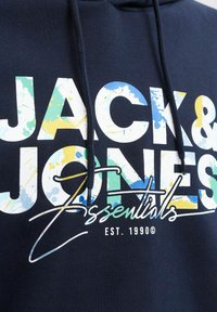 Marineblaue Kapuzenjacke mit einem großen weißen und mehrfarbigen grafischen Schriftzug. Mit Kordeln und dem Text "EST. 1990" am unteren Rand.