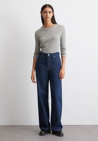 Grijze geribde longsleeve top en hooggewijde donkerblauwe wijde jeans met voorkruiszakken, gecombineerd met zwarte platte schoenen.