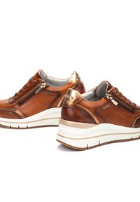 Zapatillas de cuero marrón con un acabado suave, acentos metálicos, cremalleras decorativas y una suela blanca gruesa con detalles en marrón claro.