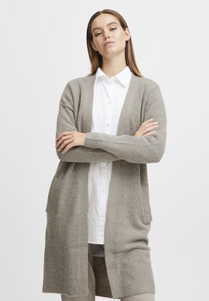 Hellgrauer Cardigan aus strukturiertem Strickstoff, mit offenem Vorderteil, langen Ärmeln und Seitentaschen. Über einem weißen Hemd mit Knopfleiste getragen.