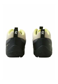 Para czarnych i beżowych sneakersów z żółtą podszewką, czarnymi uchwytami na pięcie i teksturowanymi gumowymi podeszwami, przedstawiona od tyłu.