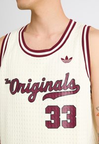 Bela mrežasta košarkaška majica s maroon naglasima, s natpisom "The Originals" i brojem 33. Adidas logo iznad natpisa.
