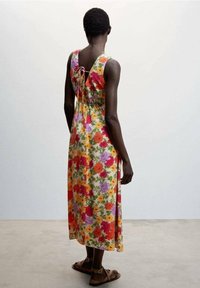 Robe maxi florale avec un dos en V, présentant un motif multicolore de fleurs rouges, roses, oranges et violettes sur un fond vert clair.