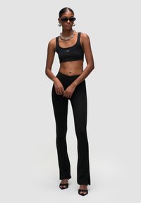 Zwart geribbelde crop top gecombineerd met hoge zwarte flared leggings. Accessoires omvatten grote ronde oorbellen en strakke zwarte zonnebril.