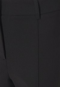 Czarne spodnie o gładkiej, matowej fakturze z dopasowanym krojem. Posiadają boczne kieszenie oraz staranne przeszycia wzdłuż szwów.